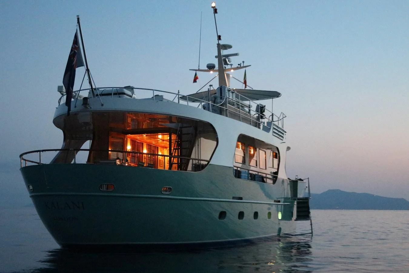 A yacht is anchored at dusk, with warm interior lights glowing invitingly. aboard KALANI Yacht for Sale