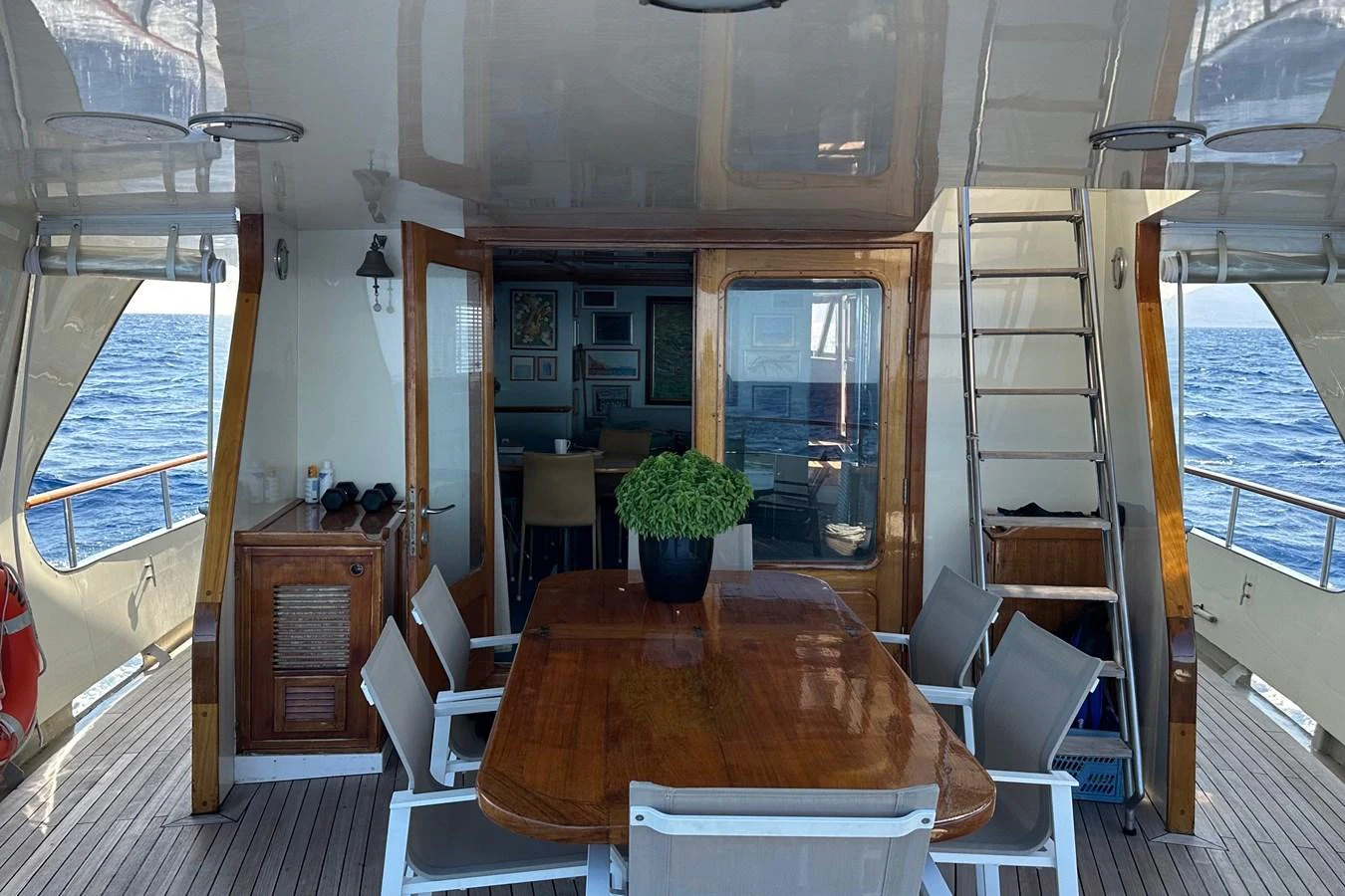 The aft deck features a polished wooden dining table surrounded by comfortable seating, perfect for alfresco dining with a view of the sea. aboard KALANI Yacht for Sale