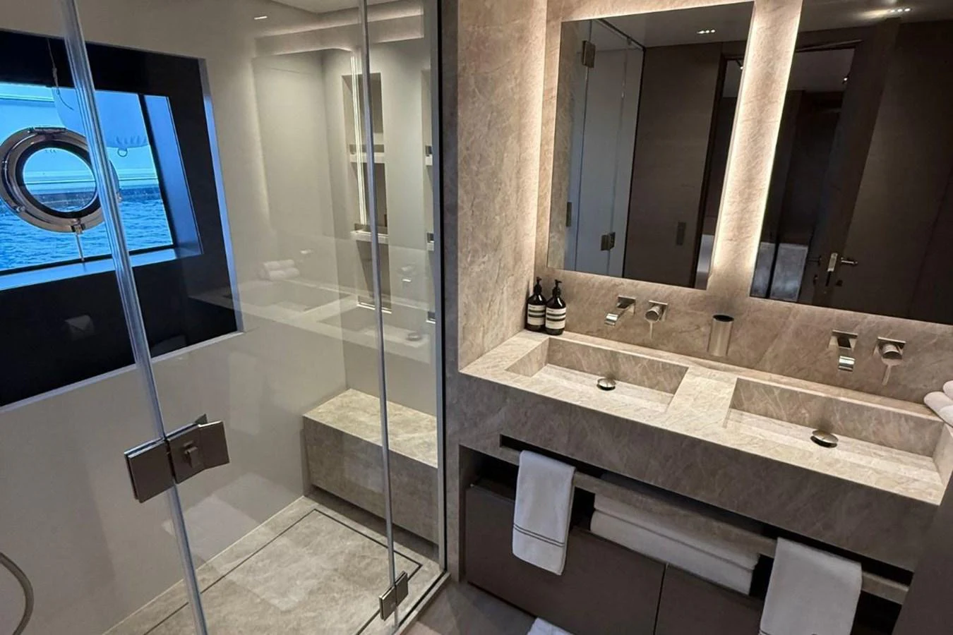A luxurious yacht bathroom featuring a double sink vanity and a spacious glass-enclosed shower with a view of the sea. aboard ALBUS Yacht for Sale