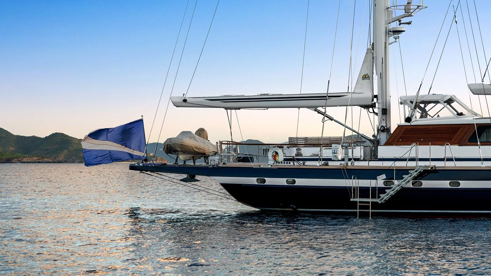 A sleek yacht is anchored on calm waters with a scenic backdrop of distant hills. aboard ISLANDIA Yacht for Sale