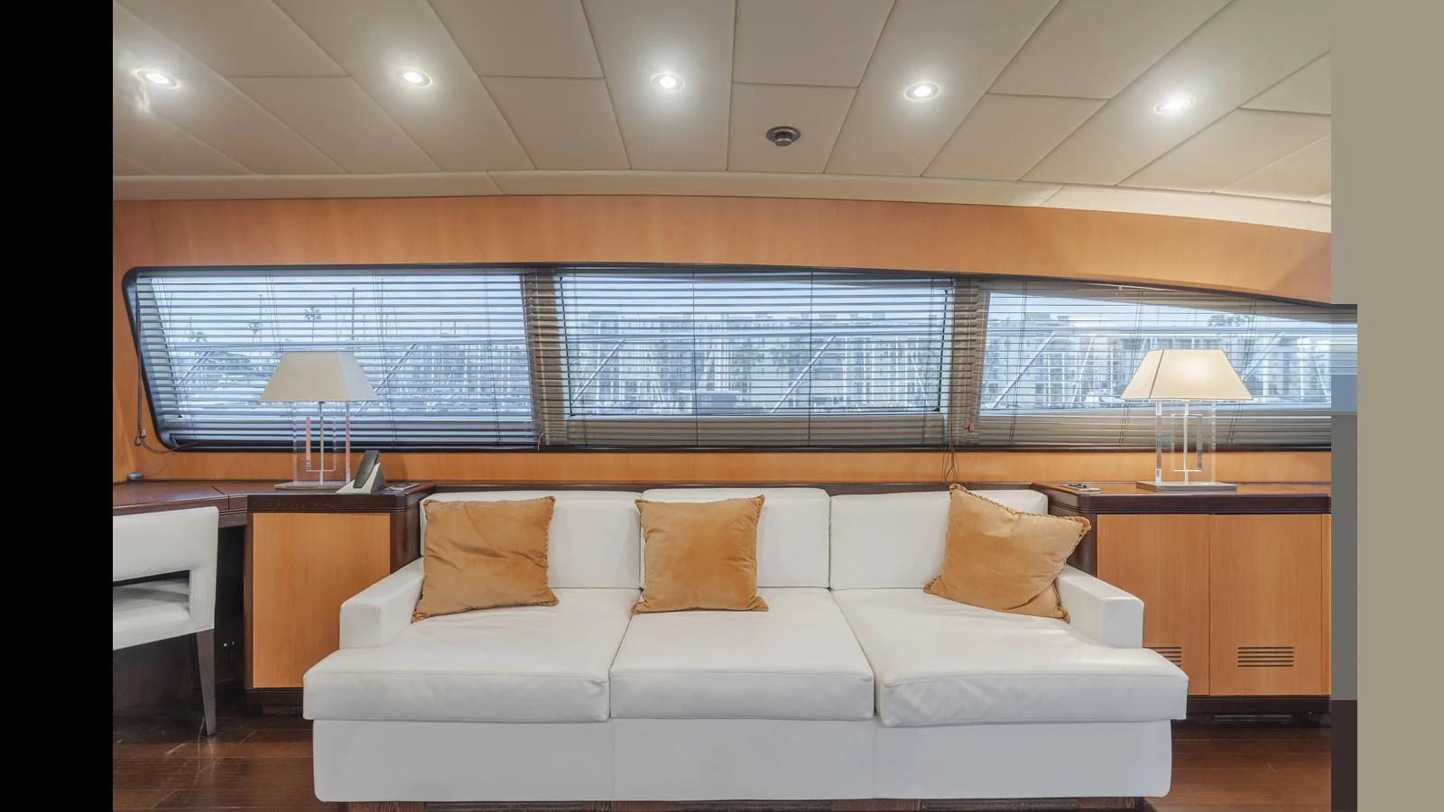 The salon features a comfortable white sofa with accent pillows, complemented by warm wooden paneling and large windows. aboard SAIGON Yacht for Sale