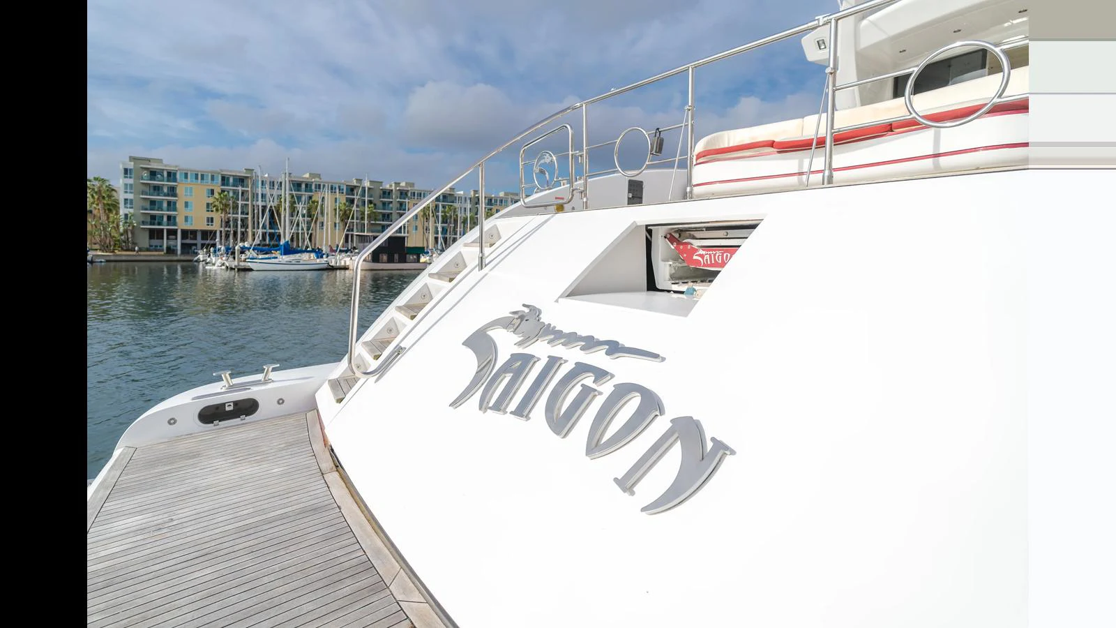 The yacht's stern showcases its name with a backdrop of a marina and modern buildings. aboard SAIGON Yacht for Sale