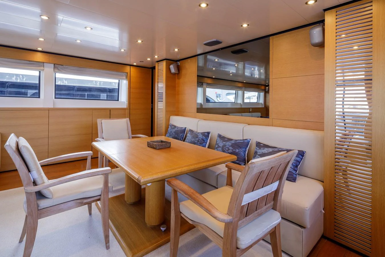 The salon features a cozy seating area with a wooden table and chairs, complemented by soft lighting and large windows. aboard BOLARO Yacht for Sale
