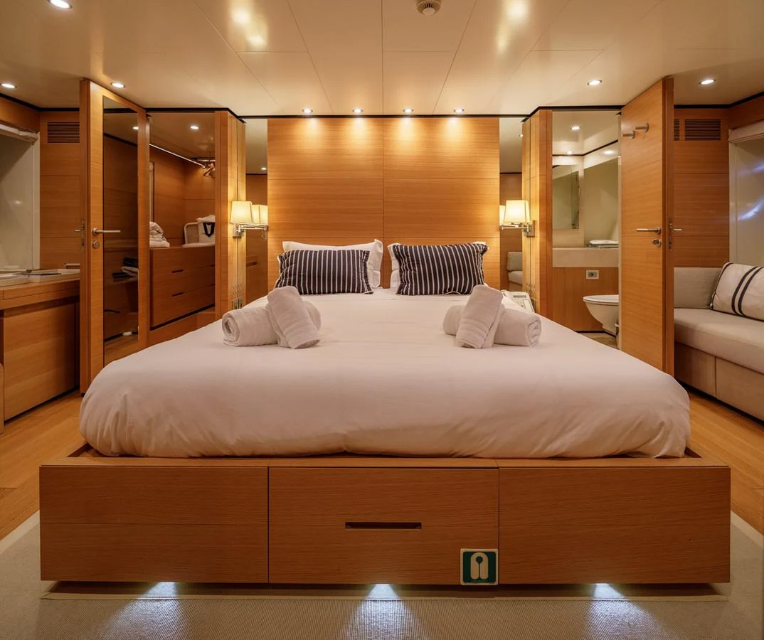 The master stateroom features a luxurious bed with elegant wood paneling and ambient lighting. aboard BOLARO Yacht for Sale