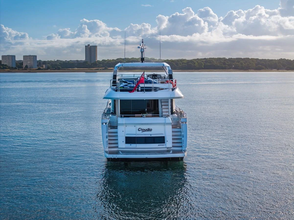 A sleek yacht is anchored on calm waters with a scenic shoreline in the background. aboard CLOUDIA Yacht for Sale