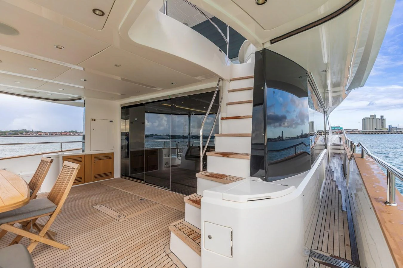The aft deck features a spacious seating area with a wooden dining table and stairs leading to the upper deck. aboard CLOUDIA Yacht for Sale