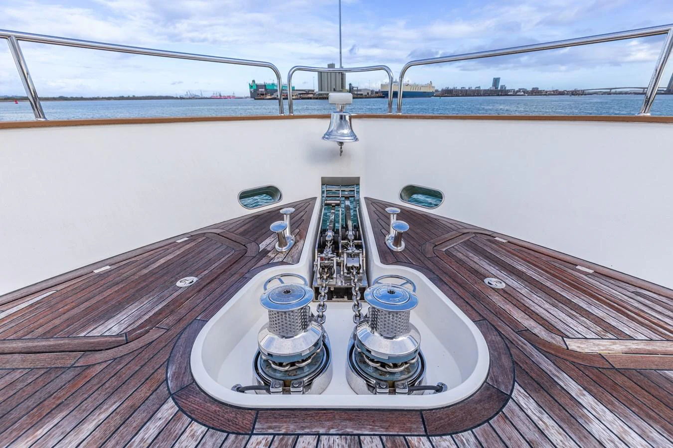 The foredeck showcases polished winches and a bell, set against a backdrop of a serene harbor. aboard CLOUDIA Yacht for Sale
