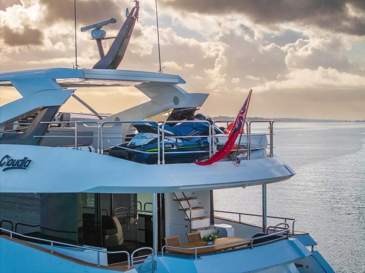 The yacht's aft deck features a jet ski and an inviting outdoor dining area, set against a serene water backdrop. aboard CLOUDIA Yacht for Sale