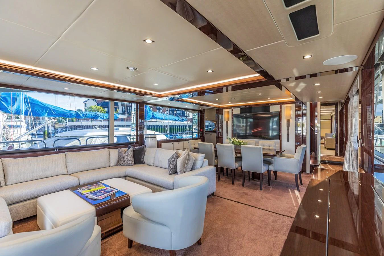 The spacious salon features elegant seating and a dining area with large windows offering stunning marina views. aboard CLOUDIA Yacht for Sale