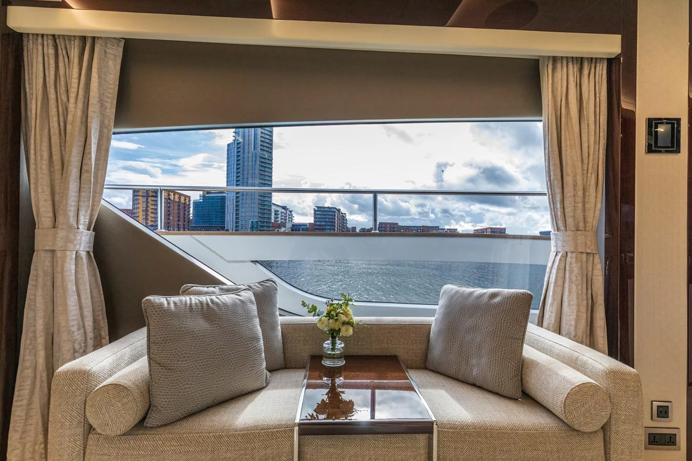 A cozy seating area with a large window offering a scenic view of the city skyline and water. aboard CLOUDIA Yacht for Sale