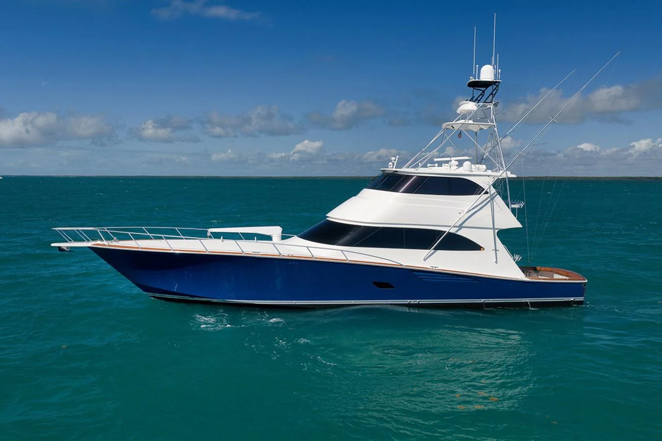 A sleek yacht with a modern design cruises on calm, turquoise waters under a clear blue sky. aboard REEL HAWK Yacht for Sale