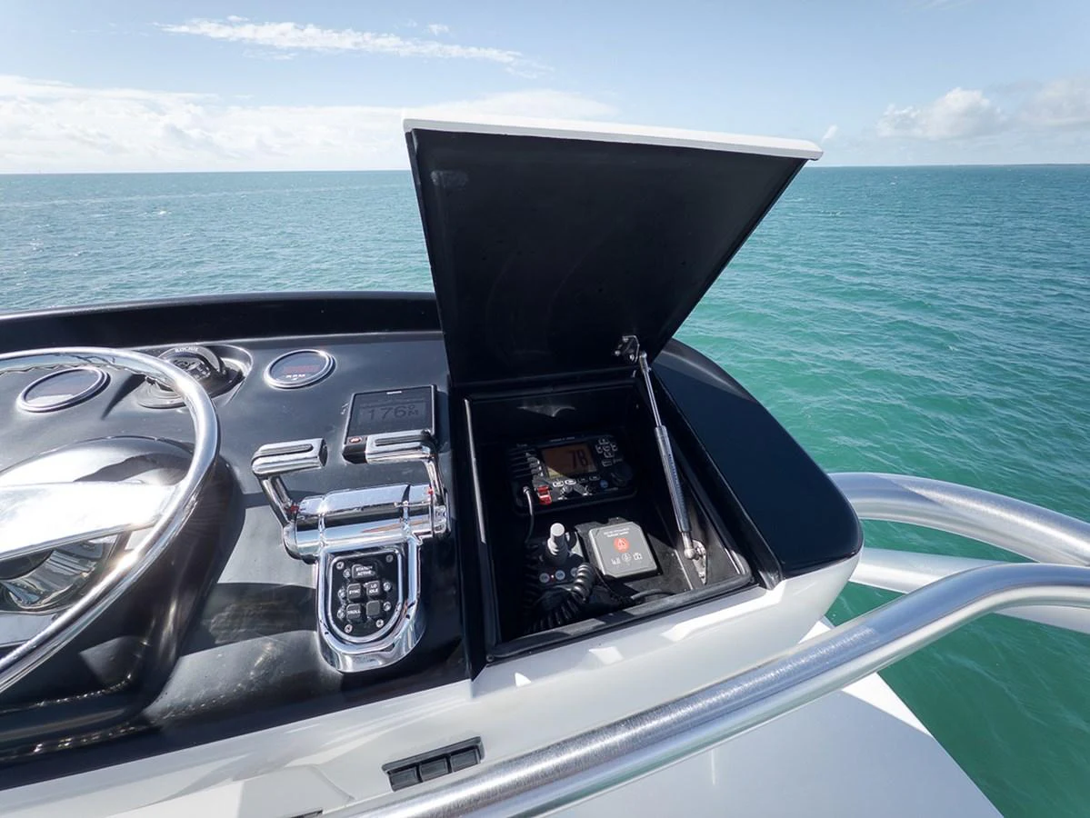 The image showcases the helm station with navigational controls and an open compartment against a serene ocean backdrop. aboard REEL HAWK Yacht for Sale