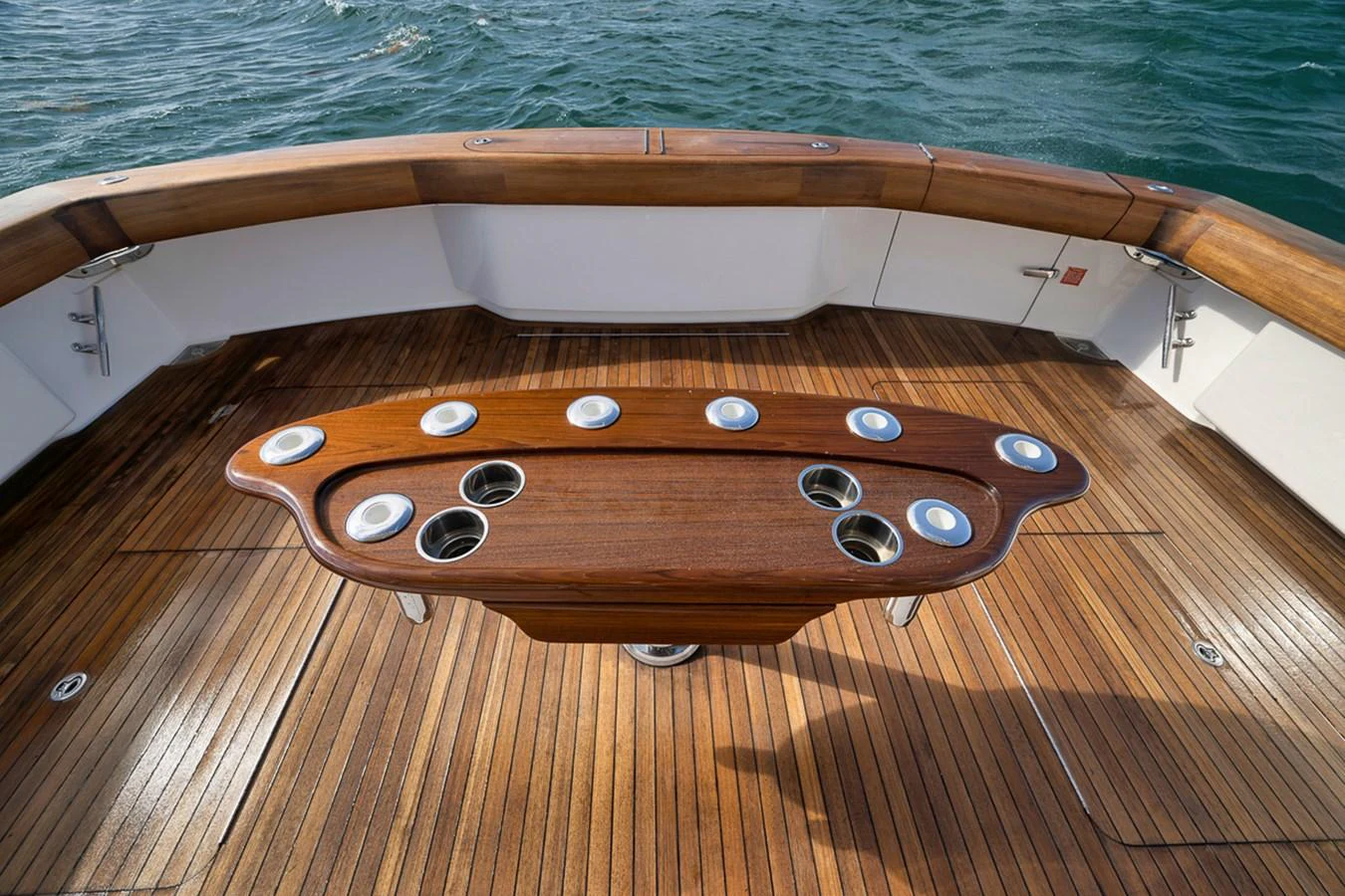 The yacht's aft deck features a beautifully crafted wooden table with integrated cup holders, surrounded by elegant teak decking. aboard REEL HAWK Yacht for Sale
