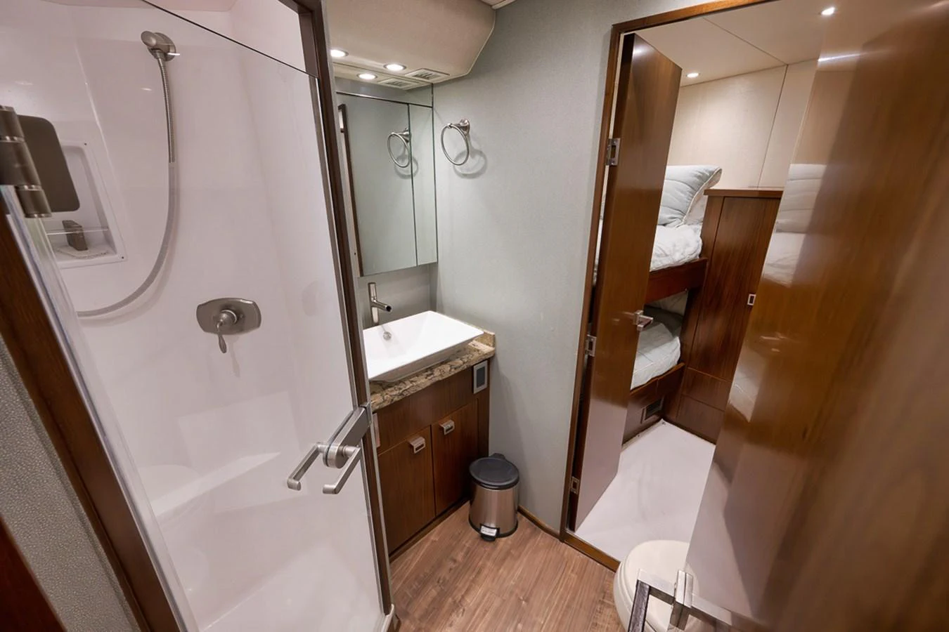 The yacht's bathroom features a modern shower, a sleek sink, and a view into a cozy bunk room. aboard REEL HAWK Yacht for Sale