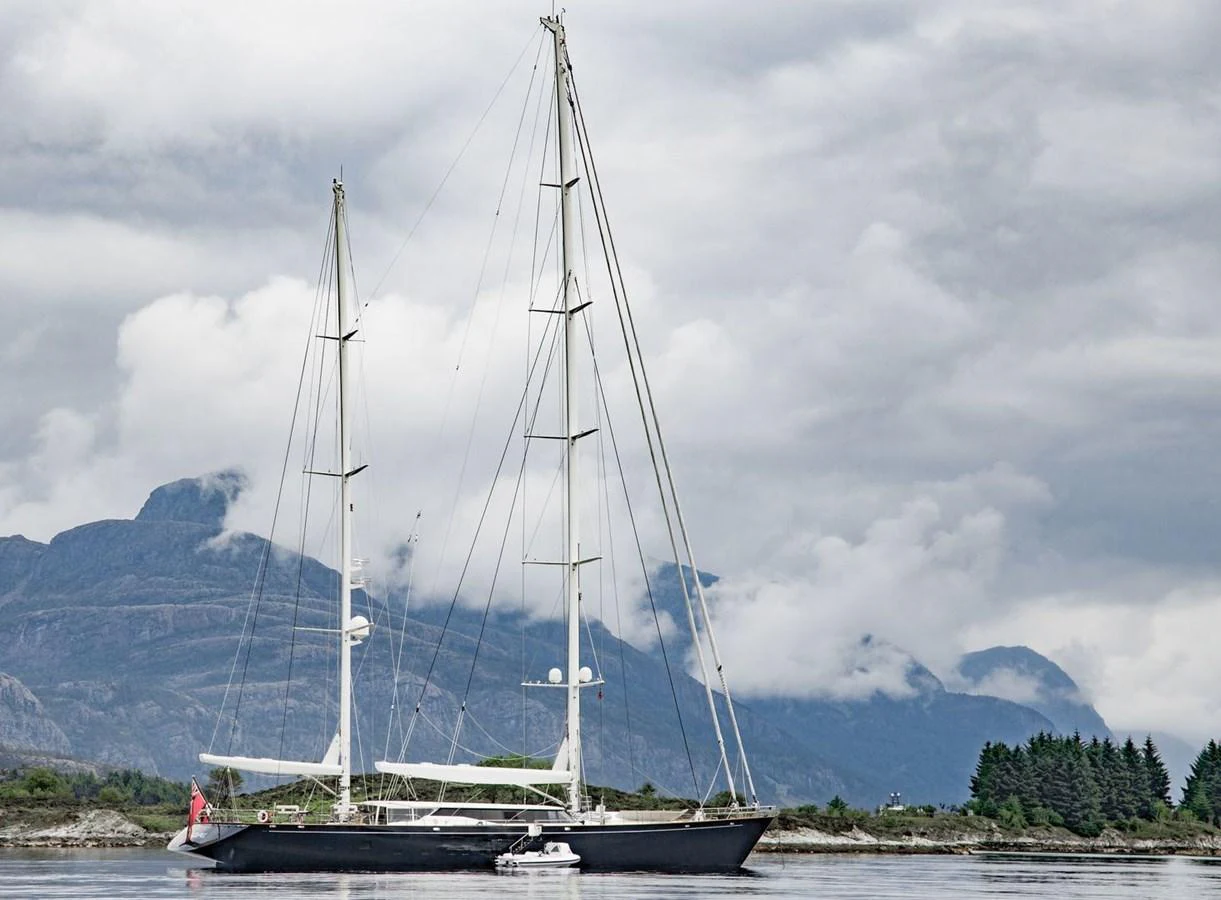 A sleek sailing yacht glides gracefully on calm waters with a mountainous backdrop. aboard SQUALL Yacht for Sale