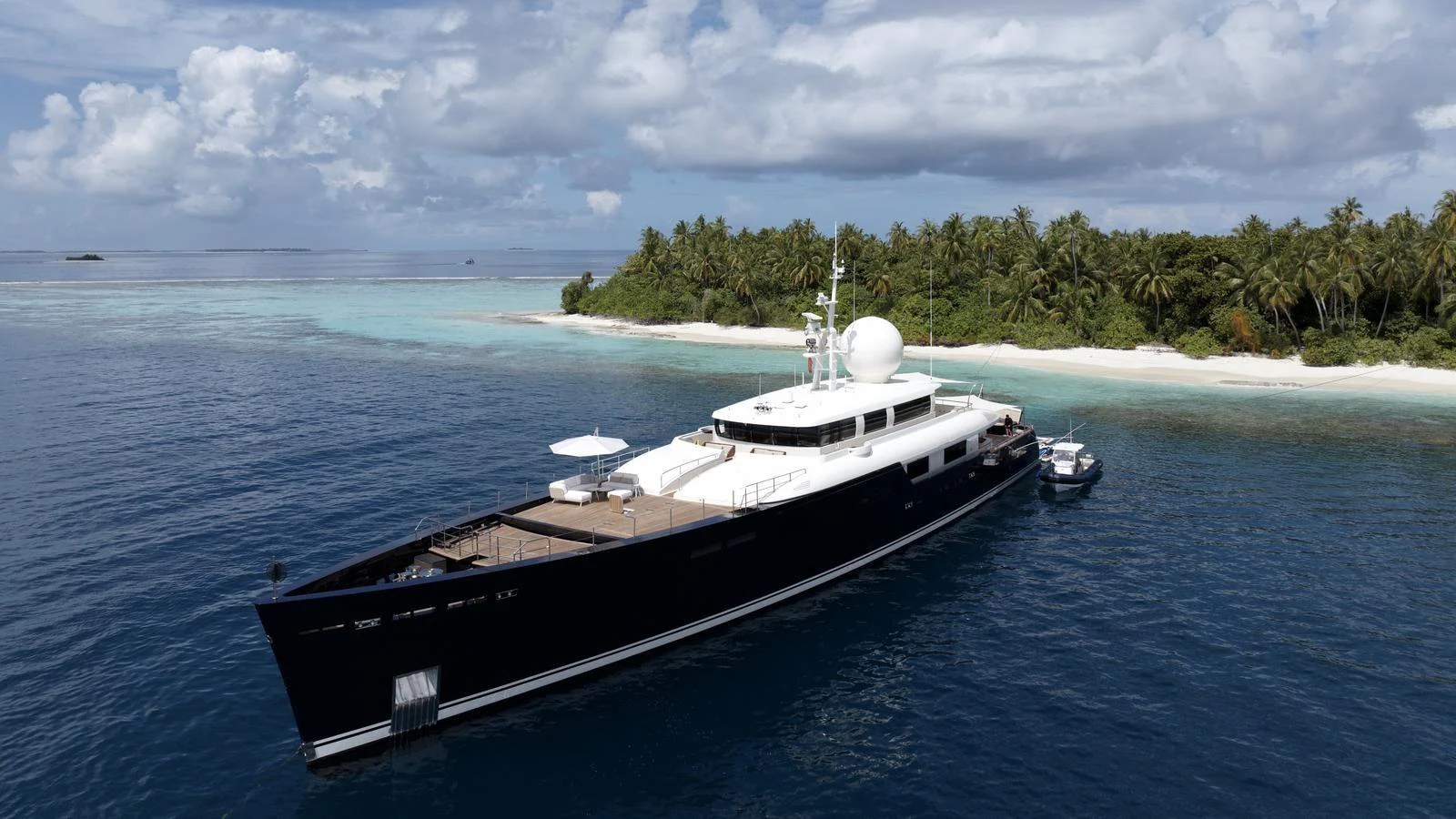 A sleek yacht is anchored near a tropical island with lush greenery and clear blue waters. aboard GALILEO Yacht for Sale