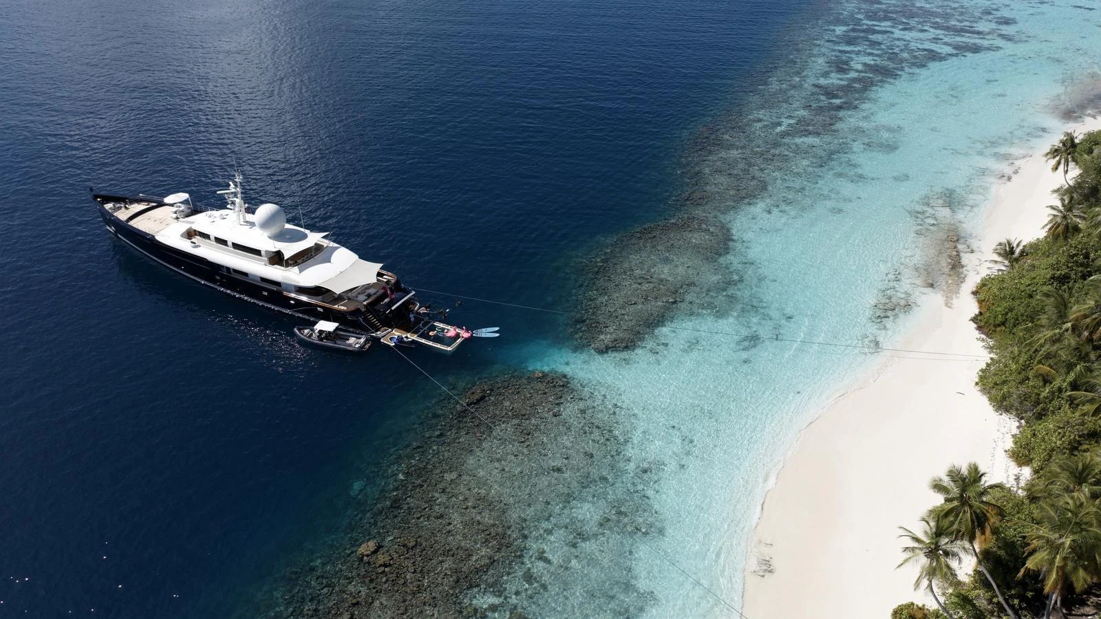 A luxurious yacht is anchored near a pristine beach with crystal-clear waters and lush greenery. aboard GALILEO Yacht for Sale