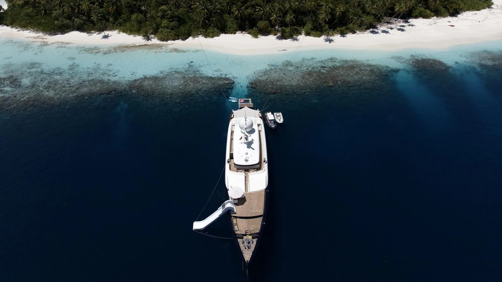 A stunning yacht anchored near a pristine tropical island with clear blue waters and lush greenery. aboard GALILEO Yacht for Sale