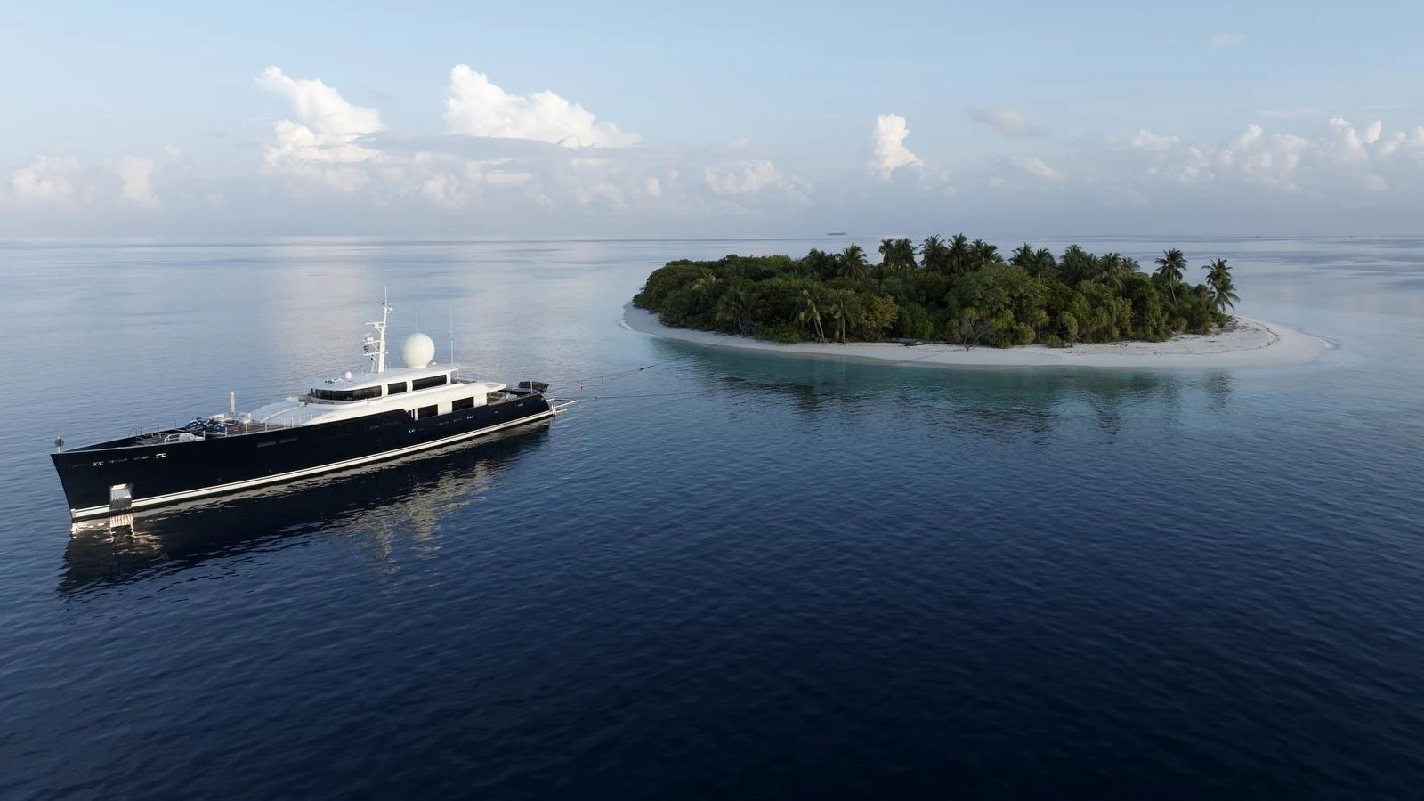 A sleek yacht cruises near a picturesque tropical island, showcasing its elegant design against a serene backdrop. aboard GALILEO Yacht for Sale