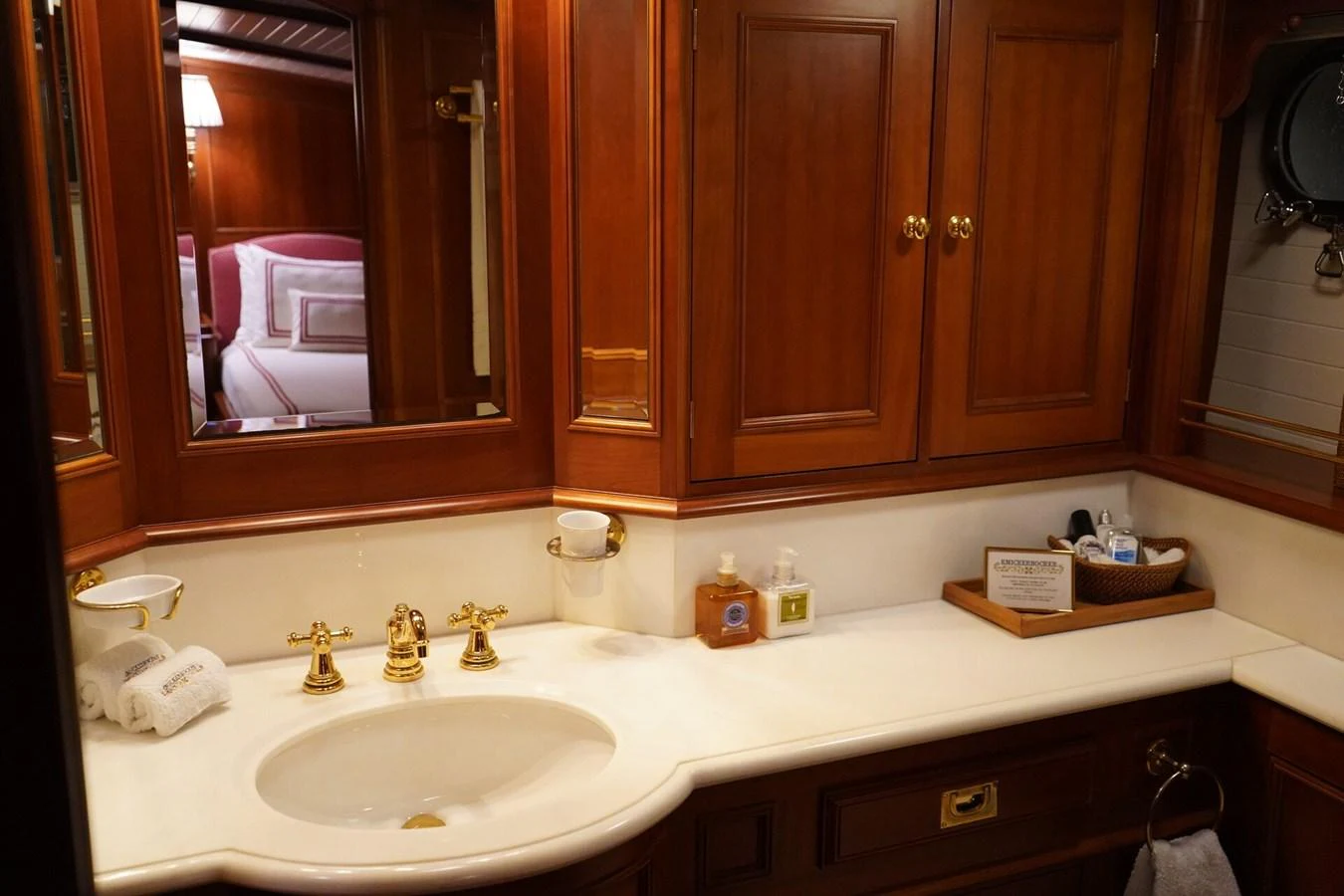 The yacht's bathroom features elegant wooden cabinetry and a pristine white countertop with gold fixtures. aboard KNICKERBOCKER Yacht for Sale