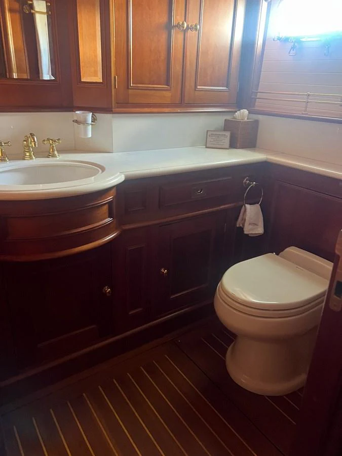 The yacht's head features elegant wooden cabinetry and a pristine white sink and toilet. aboard KNICKERBOCKER Yacht for Sale