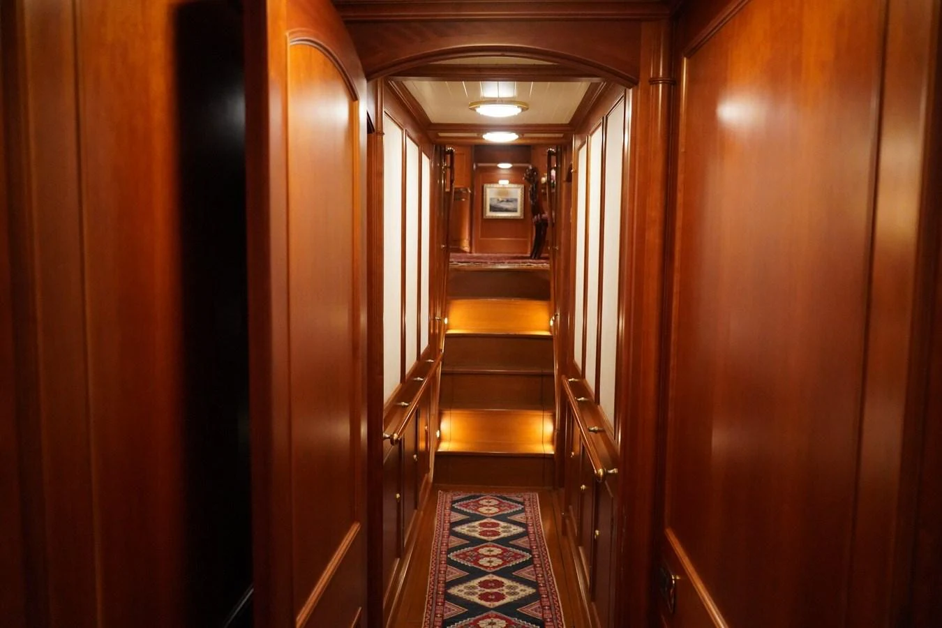 A warm, wood-paneled hallway with soft lighting and a patterned carpet runner. aboard KNICKERBOCKER Yacht for Sale