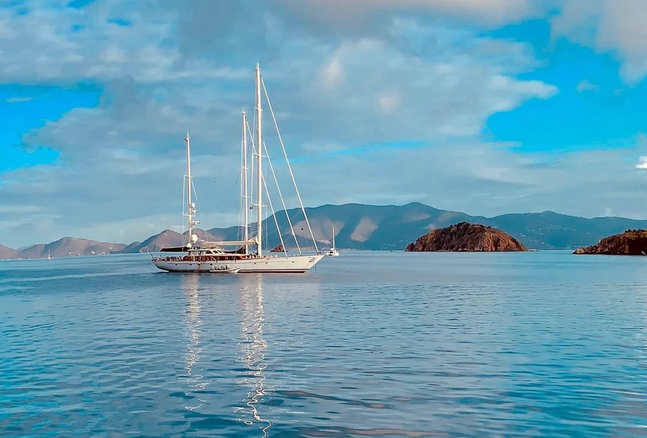A stunning yacht sails gracefully on calm waters with a picturesque island backdrop. aboard KNICKERBOCKER Yacht for Sale