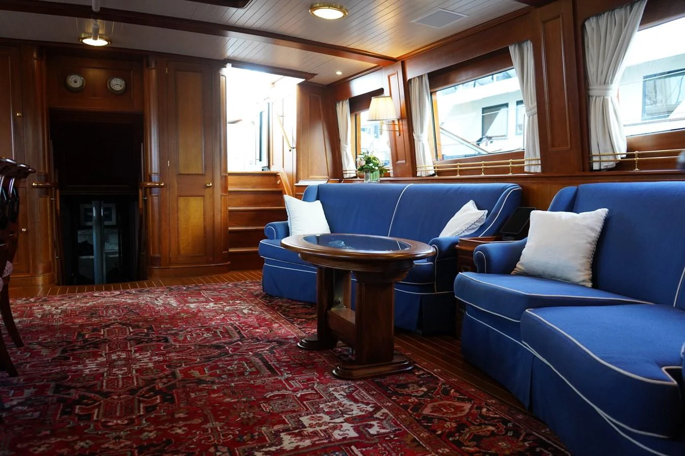 The yacht's interior features a cozy seating area with blue upholstered sofas and a richly patterned rug. aboard KNICKERBOCKER Yacht for Sale