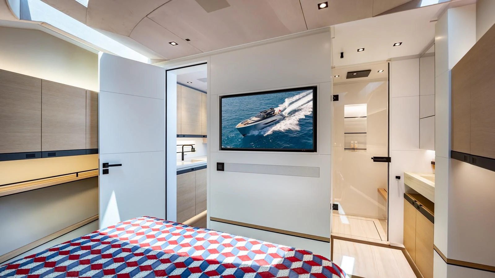 The stateroom features a modern design with a geometric-patterned bedspread and a sleek, integrated entertainment system. aboard RESOLUTE Yacht for Sale
