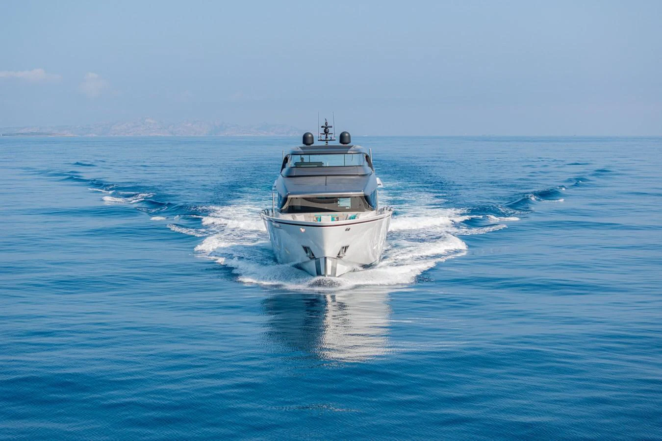 A sleek yacht cruises forward on calm, open waters under a clear blue sky. aboard M&M Yacht for Sale