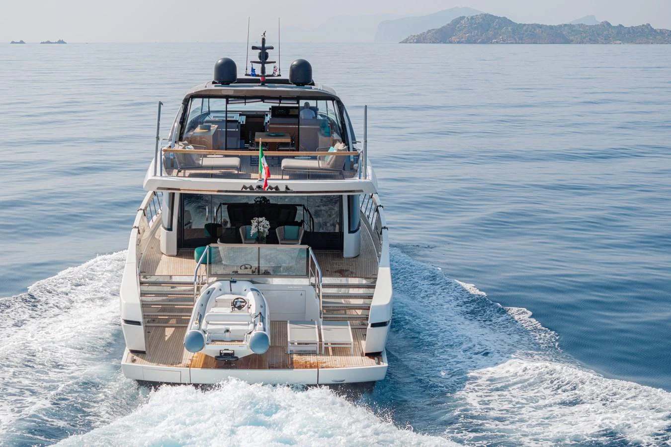 A sleek yacht cruises through calm waters, showcasing its spacious aft deck and tender. aboard M&M Yacht for Sale