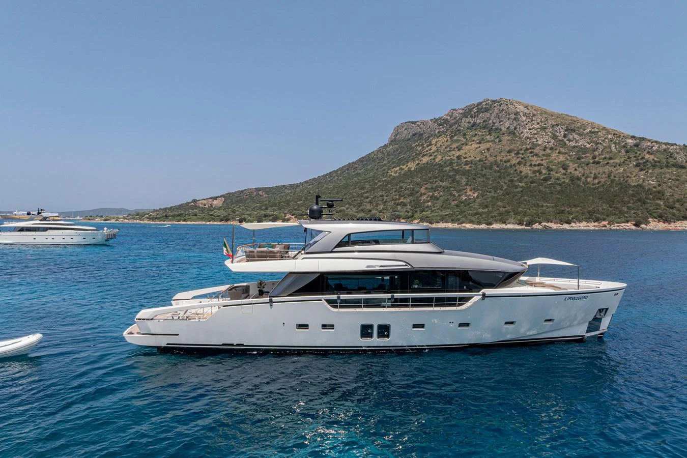 A sleek and modern yacht cruises through clear blue waters with a scenic mountainous backdrop. aboard M&M Yacht for Sale