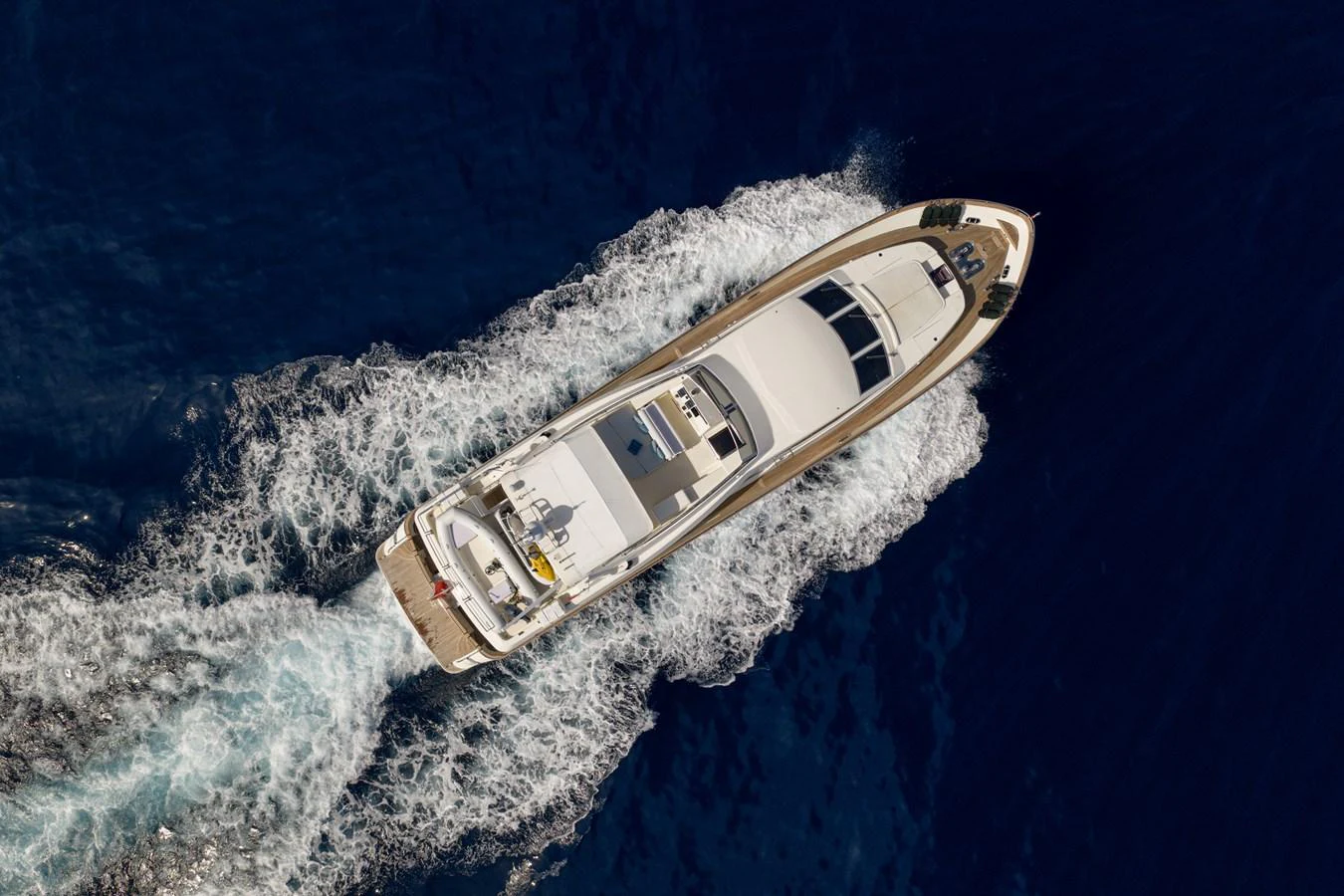 An aerial view of a sleek yacht cruising through deep blue waters, leaving a trail of white wake behind. aboard LADY MAUREEN Yacht for Sale