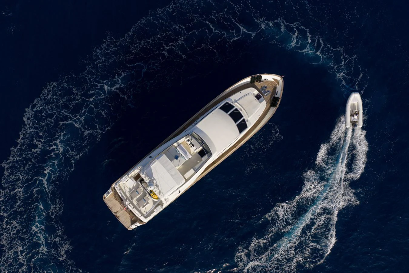 An aerial view of a luxurious yacht cruising through deep blue waters, accompanied by a small tender boat. aboard LADY MAUREEN Yacht for Sale