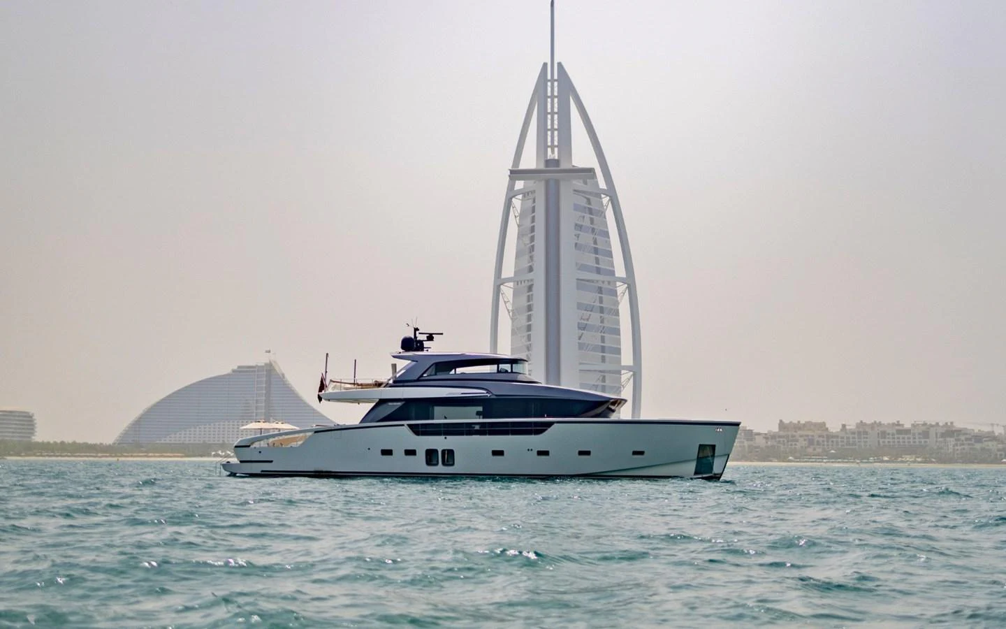 A sleek yacht cruises on calm waters with a modern architectural landmark in the background. aboard ILIA Yacht for Sale