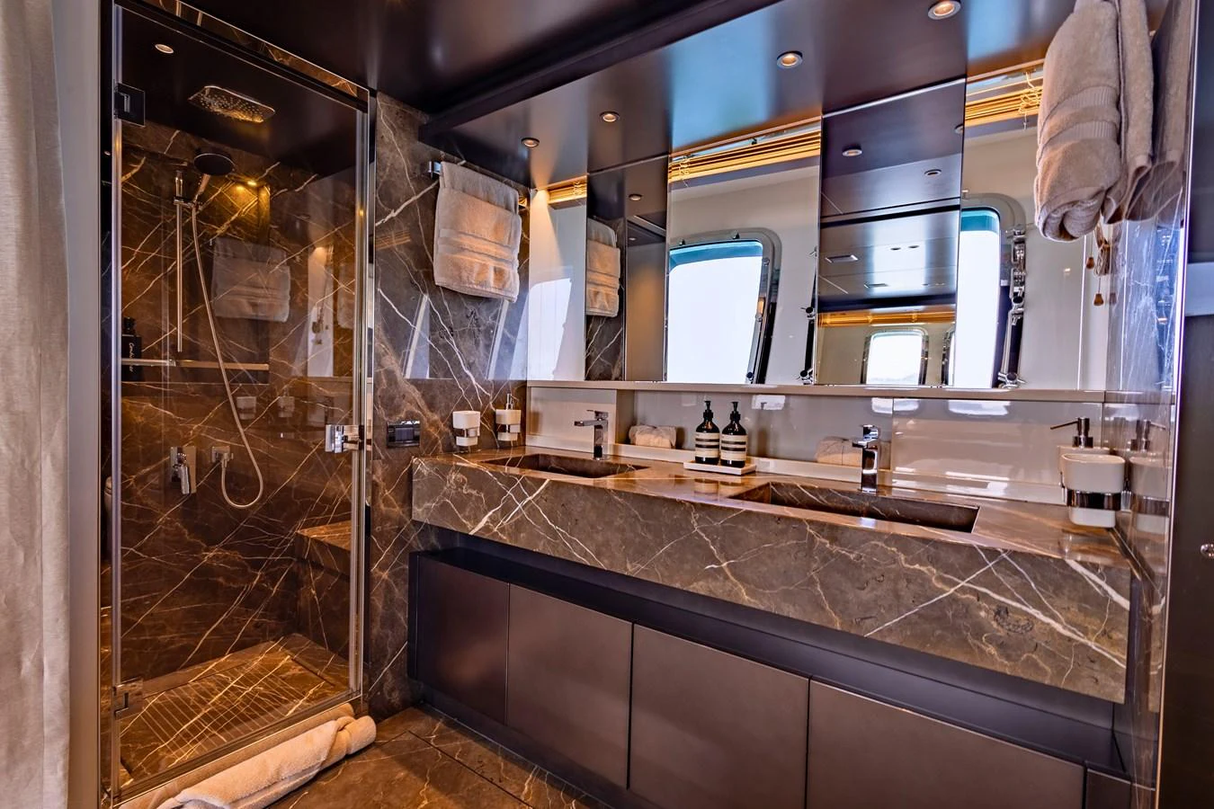 The luxurious bathroom features a double vanity with marble countertops and a spacious glass-enclosed shower. aboard ILIA Yacht for Sale