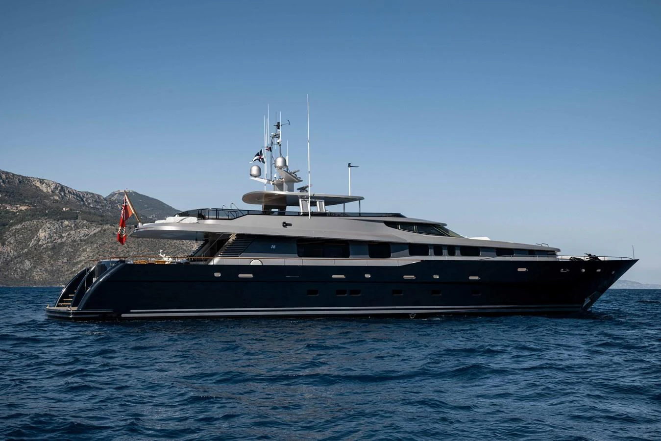A sleek and modern yacht cruising on the open water with a mountainous backdrop. aboard AURA Yacht for Sale