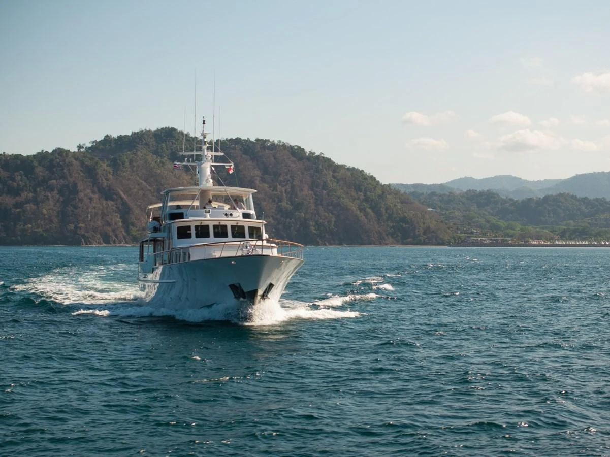 A luxurious yacht cruises through serene waters with a scenic mountainous backdrop. aboard PASSAGE Yacht for Sale
