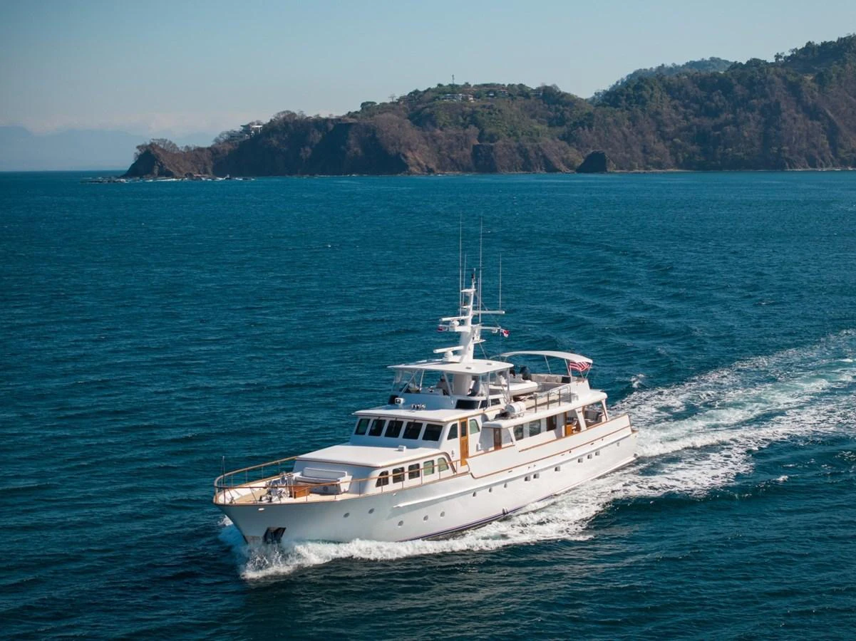 A classic yacht cruises through serene blue waters with a picturesque island in the background. aboard PASSAGE Yacht for Sale