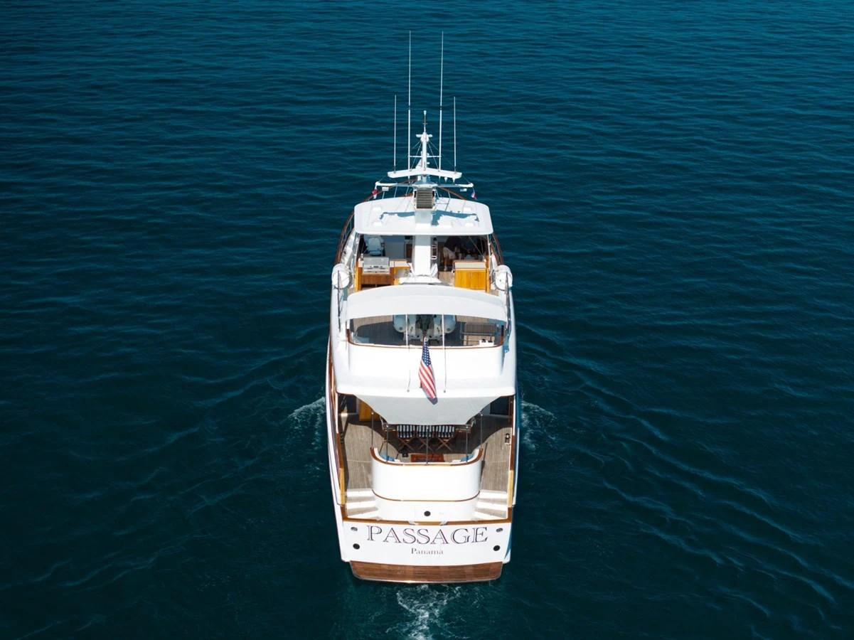 A luxurious yacht is seen from the rear, cruising through calm blue waters. aboard PASSAGE Yacht for Sale