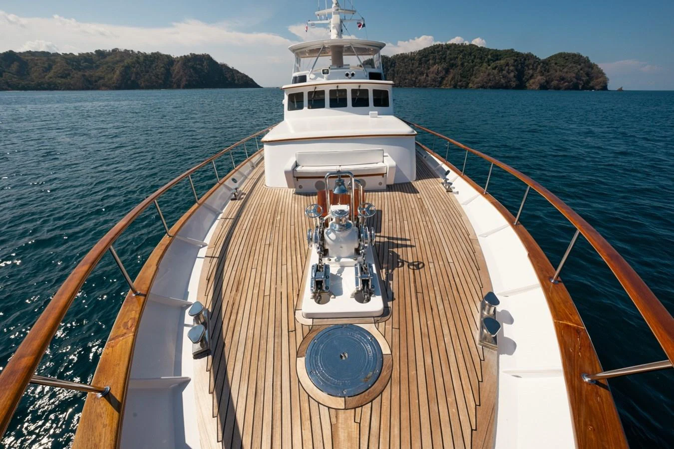 The yacht's foredeck features a spacious teak deck with polished metal fittings, set against a serene ocean backdrop. aboard PASSAGE Yacht for Sale