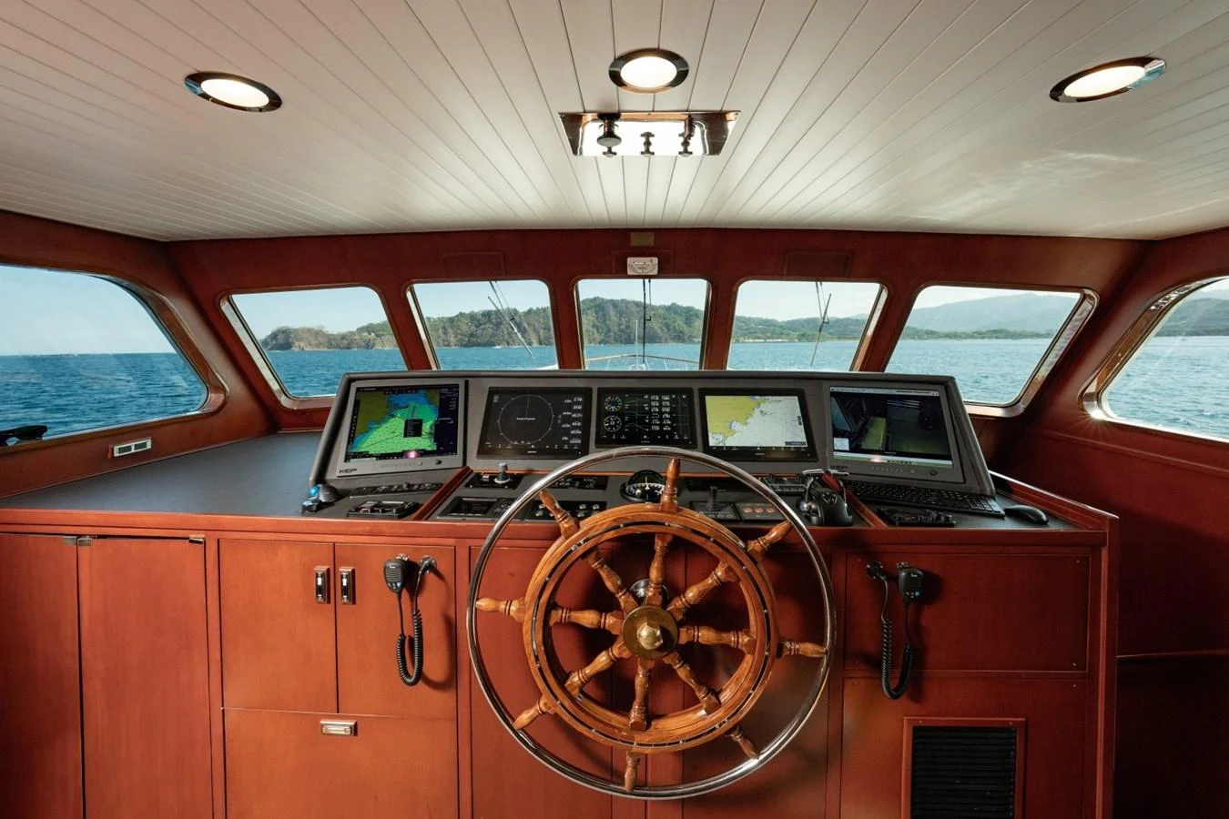 The helm features a classic wooden steering wheel and modern navigation equipment, offering a commanding view of the sea. aboard PASSAGE Yacht for Sale