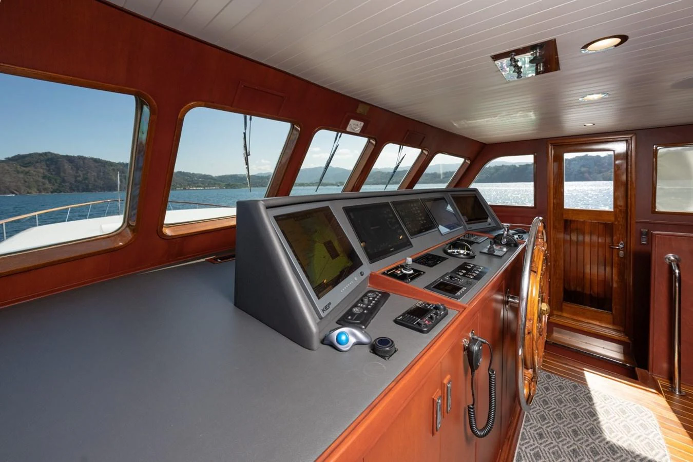 The helm station features advanced navigation equipment and a classic wooden steering wheel, offering a commanding view of the surrounding waters. aboard PASSAGE Yacht for Sale