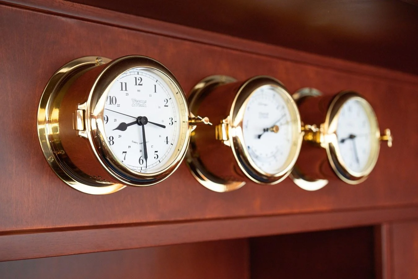 A close-up of elegant brass nautical instruments mounted on a wooden panel. aboard PASSAGE Yacht for Sale