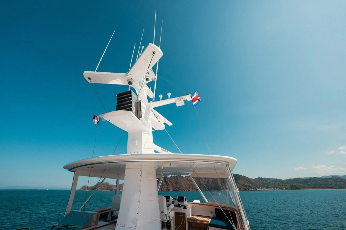 The yacht's upper deck and radar mast are showcased against a stunning coastal backdrop. aboard PASSAGE Yacht for Sale