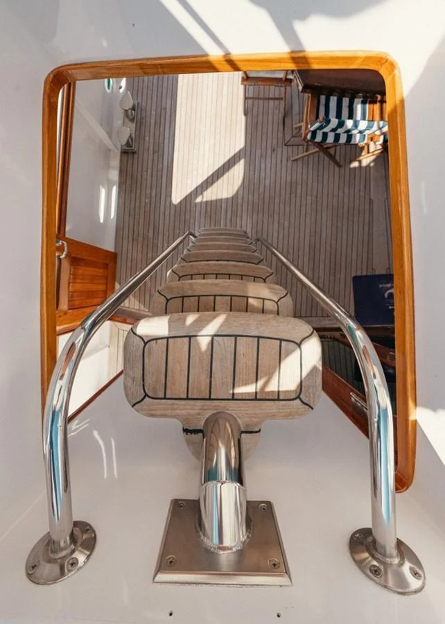 A close-up view of a yacht's ladder leading to a deck area with wooden flooring and striped cushions. aboard PASSAGE Yacht for Sale