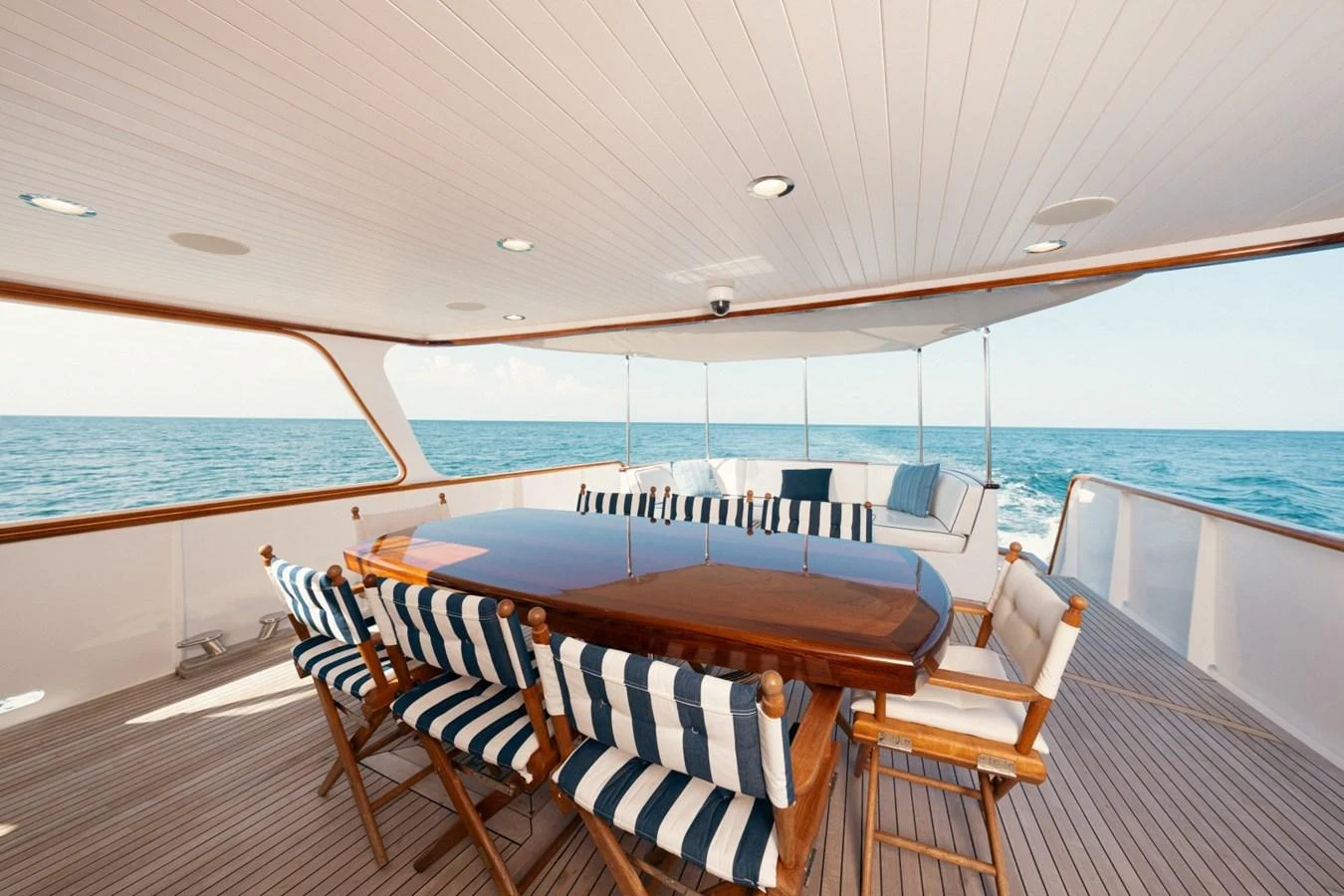 The aft deck features a spacious dining area with a polished wooden table and striped cushioned chairs, offering a perfect spot for al fresco meals with an ocean view. aboard PASSAGE Yacht for Sale