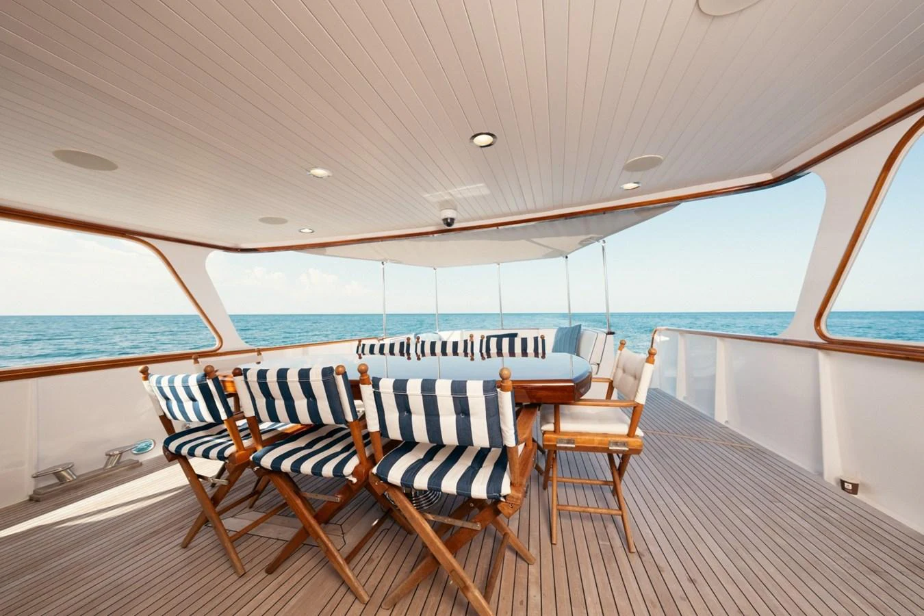 The aft deck features a spacious dining area with striped cushions and wooden chairs, offering a perfect spot for alfresco dining with a view of the sea. aboard PASSAGE Yacht for Sale