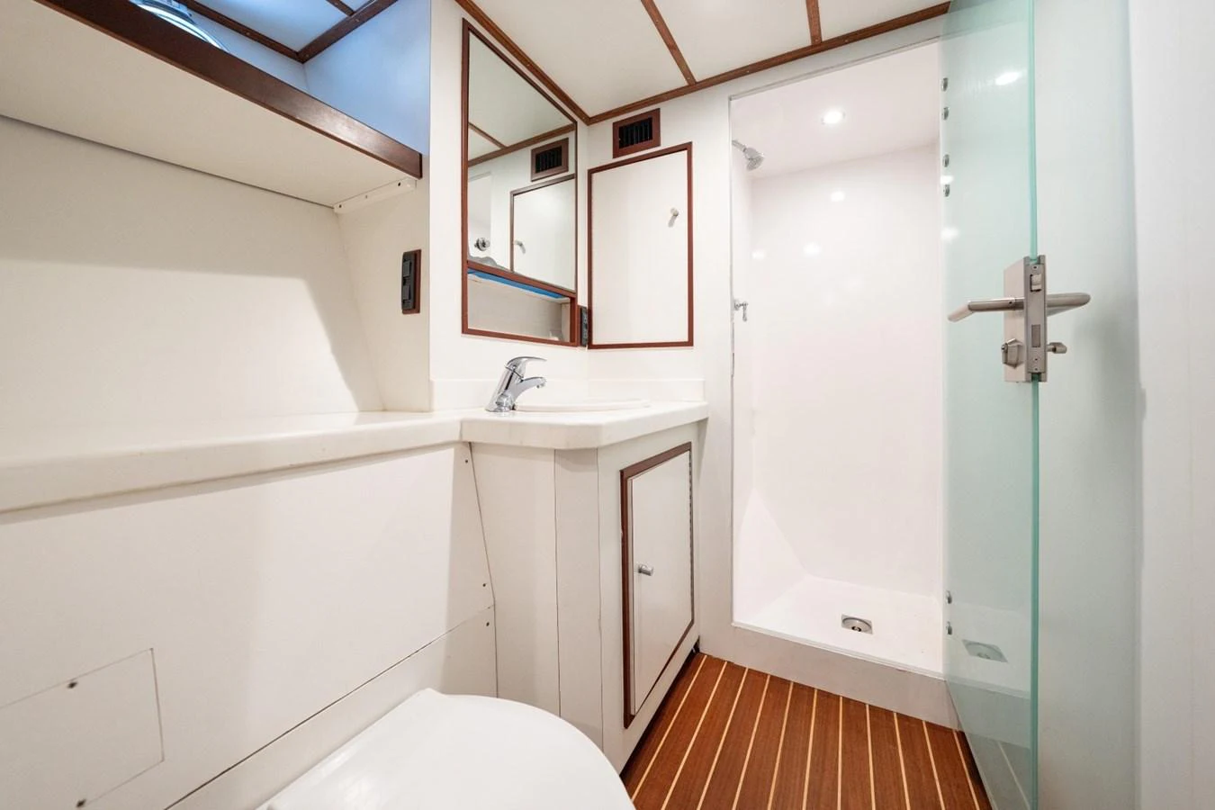 The yacht's bathroom features a sleek design with a glass shower and wooden flooring. aboard PASSAGE Yacht for Sale