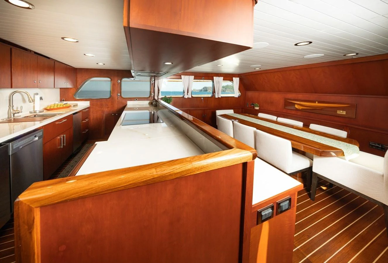 The yacht's galley features sleek wooden cabinetry, a spacious countertop, and a cozy dining area with white upholstered chairs. aboard PASSAGE Yacht for Sale